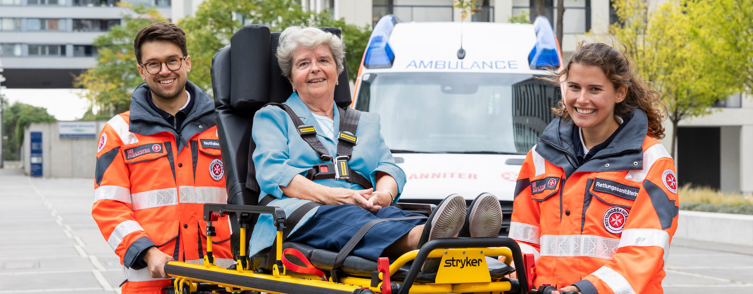 Zwei ehrenamtliche Sanitäter:innen transportieren eine Patientin auf einer Fahrtrage.