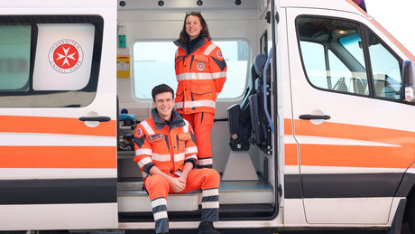 Eine Johanniterin vom FSJ steht im Krankenwagen. Ihr Kollege sitzt vor ihr in der offenen Tür.